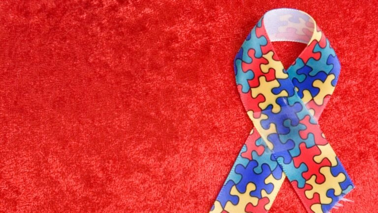 Fita com estampa colorida de quebra-cabeça, símbolo de conscientização do autismo, sobre um fundo vermelho texturizado.