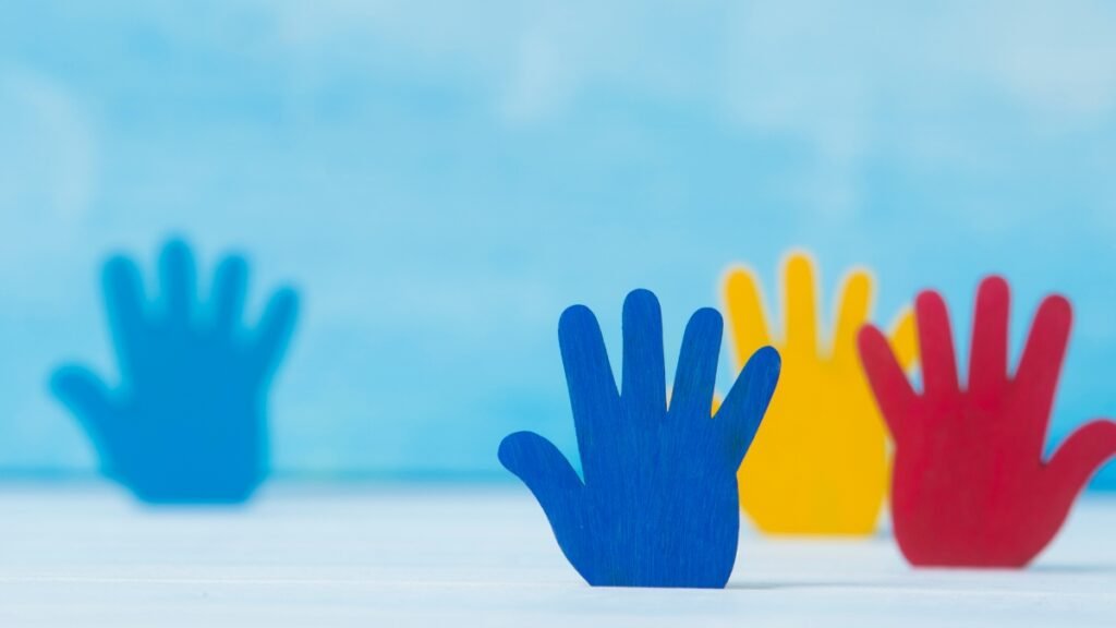 Pequenas mãos de madeira pintadas nas cores azul, amarelo e vermelho em pé contra um fundo azul claro.